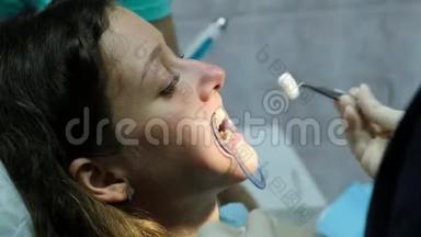 口腔科医生在妇女口腔中更换棉签，助手用牙齿聚合发光
