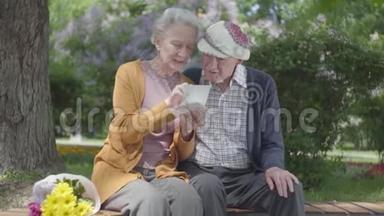 肖像可爱的成年夫妇看着老照片，回忆着坐在公园长凳上的快乐时刻。 成熟成熟