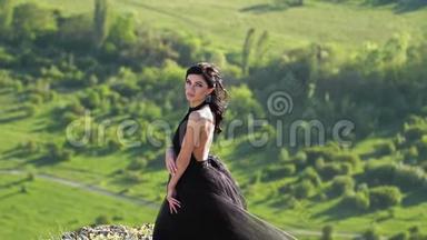 一个黑衣碧眼的年轻女子站在悬崖顶上，在绿谷的背景下摆姿势