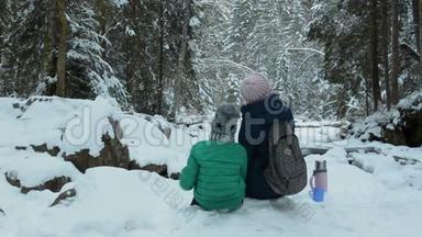 妈妈和儿子坐在一起，拥抱在白雪覆盖的森林里。 冬季<strong>阴天</strong>。 后景。