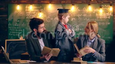 一个穿着夹克和毕业帽的男孩和两个在学校<strong>班级</strong>背景下拿着书的老师交流