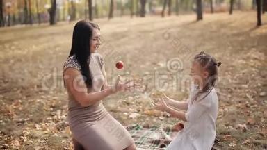快乐的妈妈和<strong>女儿</strong>在城市公园玩得很开心。 <strong>一家人</strong>笑着，互相扭打苹果。