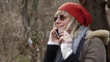 年轻漂亮的女人，戴着红帽子坐在树旁，用手机说话