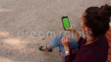 年轻漂亮的<strong>女孩</strong>坐在公园的长凳上，在智能手机上浏览<strong>社交网络</strong>。