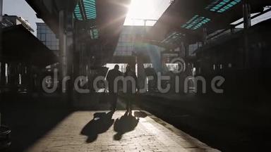 两个带着旅行袋的男人在最后<strong>一缕</strong>阳光下在火车站的月台上交谈