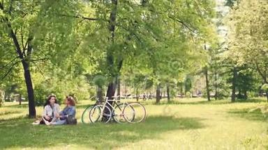 两个漂亮的女孩朋友正在公园的草坪上谈笑风生，天气晴朗，夏天。 现代自行车