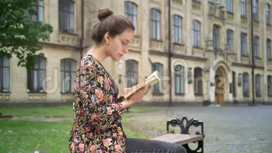 年轻漂亮的女大学生在大学附近的街道上读书，看书，坐在长凳上