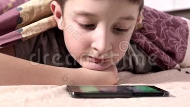一个男孩躺在家里的床上，在智能手机上放松和<strong>观看视频</strong>
