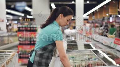 穿着围裙的漂亮女售货员正忙着把袋子和预先煮熟的食物放进冰箱。 货架上的鲜艳产品