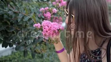 一个年轻的女孩走在一个夏天的公园里，弯下腰去感受美丽的粉红色花朵的气味，这种气味令人不快