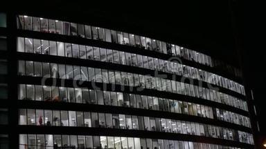 晚上大型办公楼.. 有灯光的窗户。 人们完成这项工作。 从底部看。