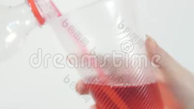 一个女人把一个塑料瓶里的红色<strong>水果</strong>饮料倒入<strong>玻璃杯</strong>里。