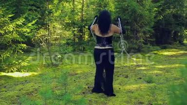 一个穿着黑色衣服的年轻女巫从锁链上挣脱出来，在森林里和他们一起旋转。 万圣节。 哥尼克风格