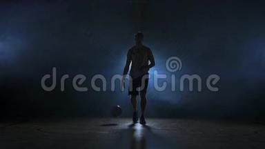 篮球运动员在一个黑暗的房间里径直走向摄像机，烟雾中有一个背光的背部看着摄像机。