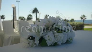 婚礼上的白色<strong>百合花</strong>和白色<strong>玫瑰花</strong>束装饰桌布在模糊阳光的度假村背景上