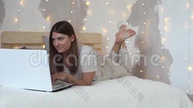 一个穿睡衣的漂亮女孩躺在床上，用笔记本电脑。 高清。 总体计划。