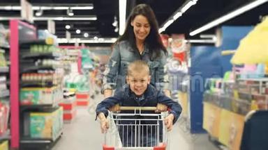 可爱的妈妈和她可爱的小儿子在超市里玩得很开心，她带着小购物车跑着