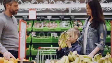 妈妈，爸爸和可爱的男孩在<strong>食品店</strong>里挑选水果，孩子在闻香蕉，把它们送给他的父亲，男人是
