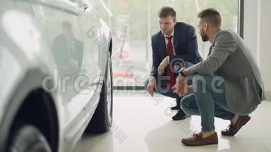 两个男人热情的顾客和友好的推销员正在交谈和手势讨论汽车模型，而蹲在附近