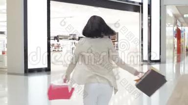 女人穿着柔软的彩色牛仔裤和夹克，双手拿着购物袋在商场里<strong>走来走</strong>去。