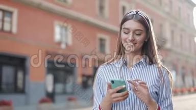 微笑的年轻女子穿着蓝色和白色条纹连衣裙，用智能手机在老街上<strong>走来走</strong>去
