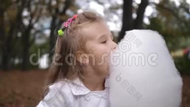 金发小女孩正在城市公园吃甜棉花糖。 美丽的小女孩在吃糖果-棉花糖。 儿童饮食