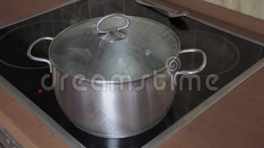 一只手从装有开水的锅盖上取下一个热盖，放在感应玻璃陶瓷炉炉的炉顶上
