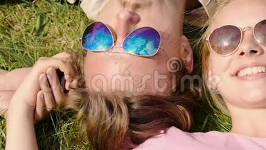 幸福的一对夫妇戴着太阳镜躺在草地上，双手捧着天空的倒影