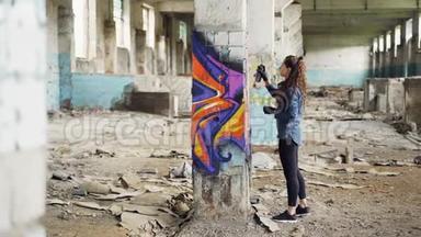 漂亮的女孩涂鸦艺术家用抽象的图片在空荡荡的工业大楼里装饰旧的损坏的柱子