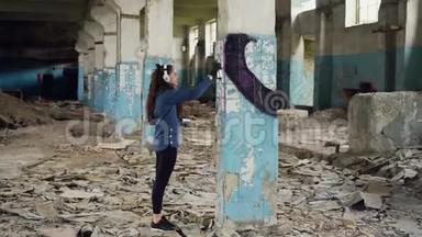 城市艺术家正在废弃的仓库里用气溶胶油漆用抽象的图像装饰<strong>柱子</strong>。 女孩穿着休闲装