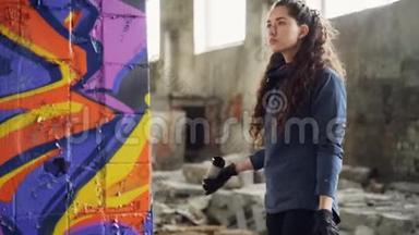 严肃的年轻女子涂鸦艺术家正在旧仓库的柱子上使用喷漆。 废弃的肮脏建筑