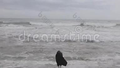一个美丽的女孩在寒冷的一天自由地跑到波浪状的大海，抚摸着水，跑回来