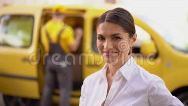 微笑的女商人正竖起大拇指。 后台模糊的送货车和快递