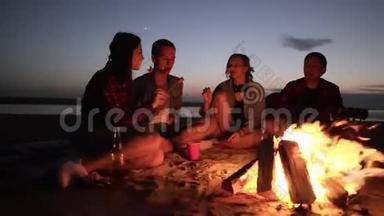 朋友们坐在篝火旁的格子布上、用木棍煎食物、吃东西的加速镜头