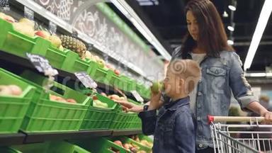 可爱的小男孩正在杂货店的果蔬部挑选苹果，他迷人的妈妈是