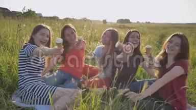 在一个温暖的夏天，五个年轻的女学生在草地上吃冰淇淋并展示冰淇淋。
