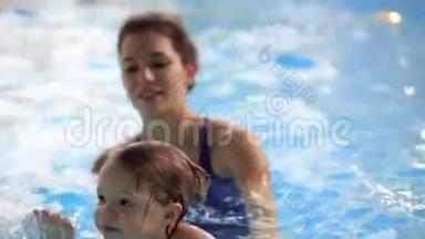 美丽的妈妈教可爱的宝贝女孩如何在游泳池里游泳。 孩子和妈妈在水里玩。