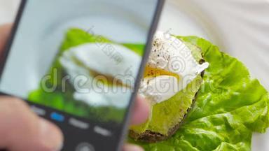 餐馆里的一个男人用手机摄像头拍摄食物。 <strong>荷包蛋</strong>三明治和鳄梨