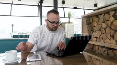 一个留胡子的年轻人，戴着眼镜，在笔记本电脑和平板电脑上工作。 休息一下，他喝咖啡。 <strong>快节奏</strong>概念