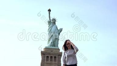 快乐微笑的欧洲女人站在镜头前，在阳光明媚的纽约慢动作中向自由女神像摆姿势。