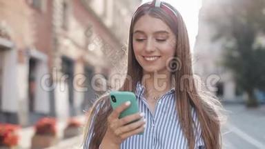 微笑的年轻女子穿着蓝色和白色条纹连衣裙，用智能手机在老街<strong>上走来走去</strong>