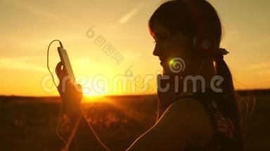 快乐的女孩在智能<strong>手机</strong>上听音乐，在美丽的<strong>春天</strong>日落的光线下。 慢动作。 年轻女孩