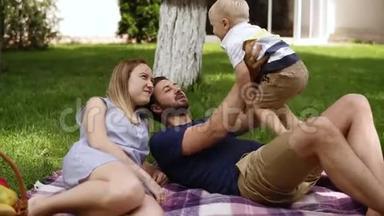 一对年轻夫妇带着一个孩子在公园草地上休息。 三口<strong>之家幸福</strong>，有一个金发的小男孩