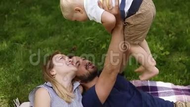 三口之家的高角度镜头。 躺在绿草上，和他的小儿子玩。 快乐生活