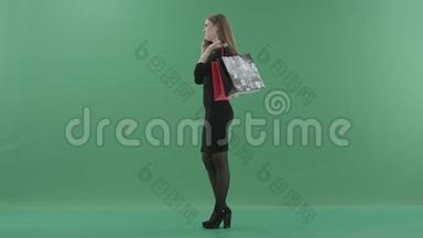 穿着小黑裙子的漂亮女人拿着购物袋在手机上说话。 她站着