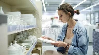 商店里的一个女孩看着白色的<strong>陶瓷盘子</strong>。 她转动手中的<strong>盘子</strong>，选择。 你看着那些