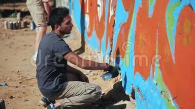涂鸦艺术家在街墙上画画。 英俊的男人和女孩用喷雾瓶喷洒五颜六色