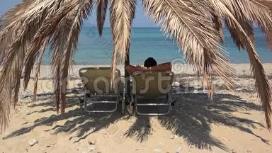 男人躺在日光浴床上的棕榈树遮阳伞下，欣赏<strong>蔚蓝</strong>的<strong>大海</strong>，在异国情调的海滩上放松度假