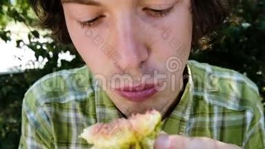 一个男人在一个夏季公园特写镜头中吃一个成熟的无花果的肖像，动作缓慢。