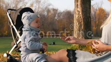 年轻的妈妈坐在草地上和她的小宝宝玩.. 向摄影师挥手